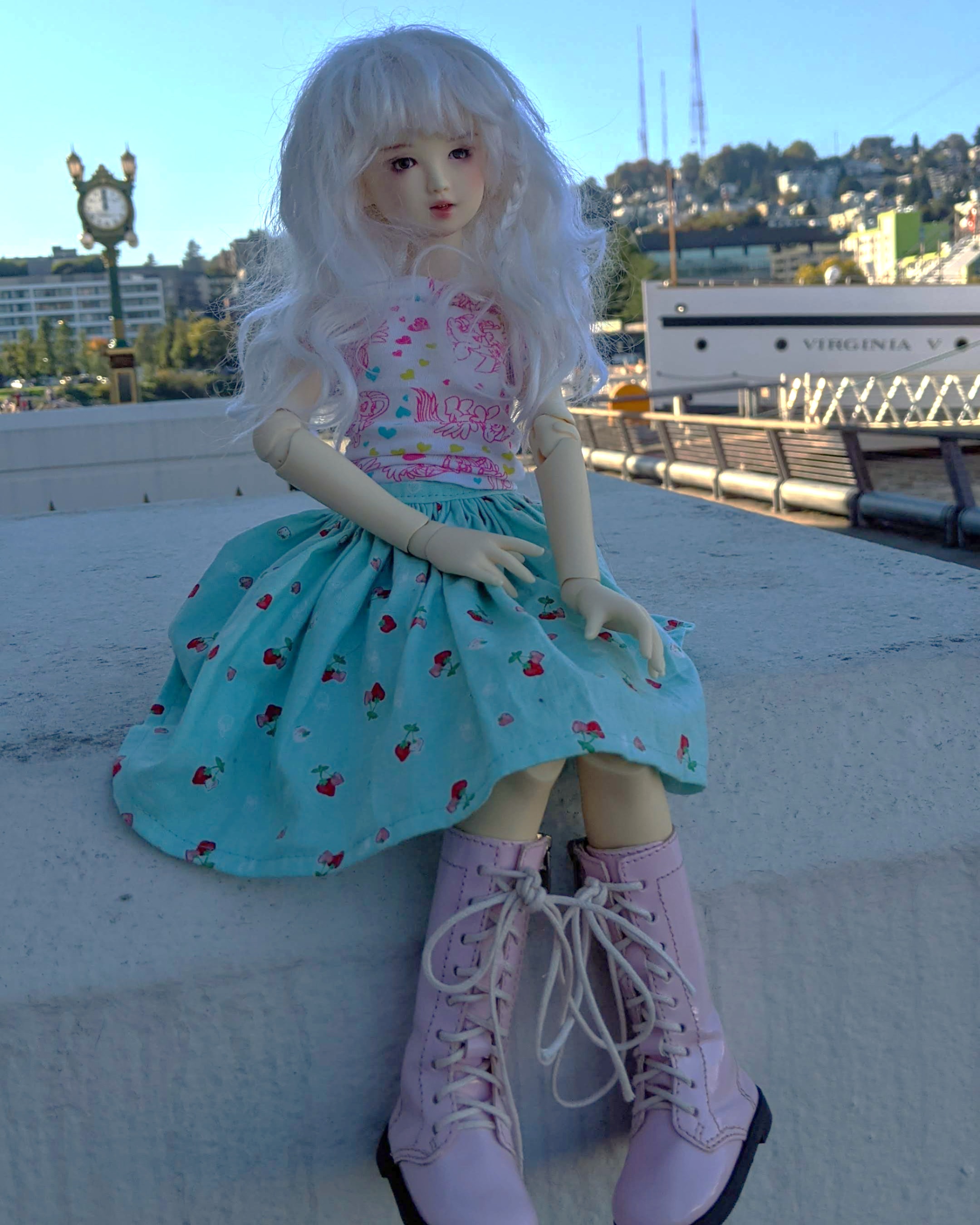 a photo of a girl doll looking up off to the right. she is white and has white hair. in the background there is a boat titled the virginia v.